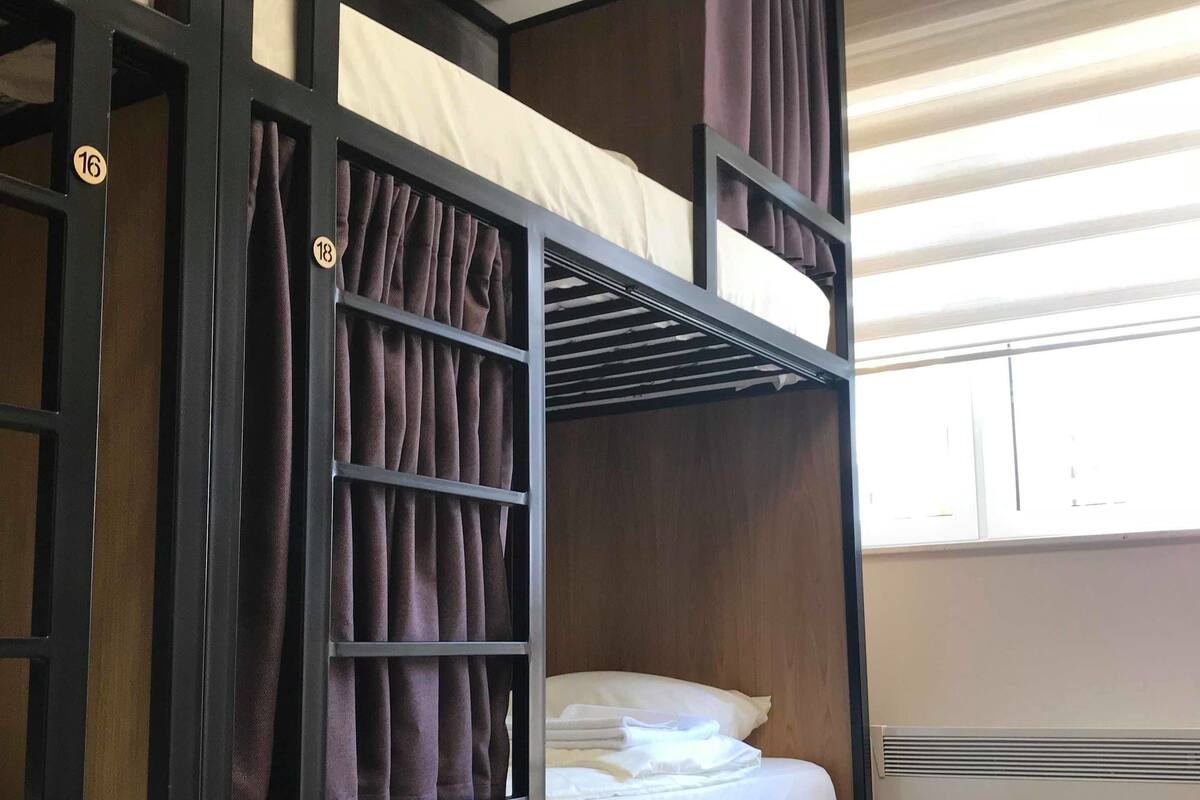 Una cama litera con estructura de madera, una ventana con persianas y un par de zapatos en el suelo.