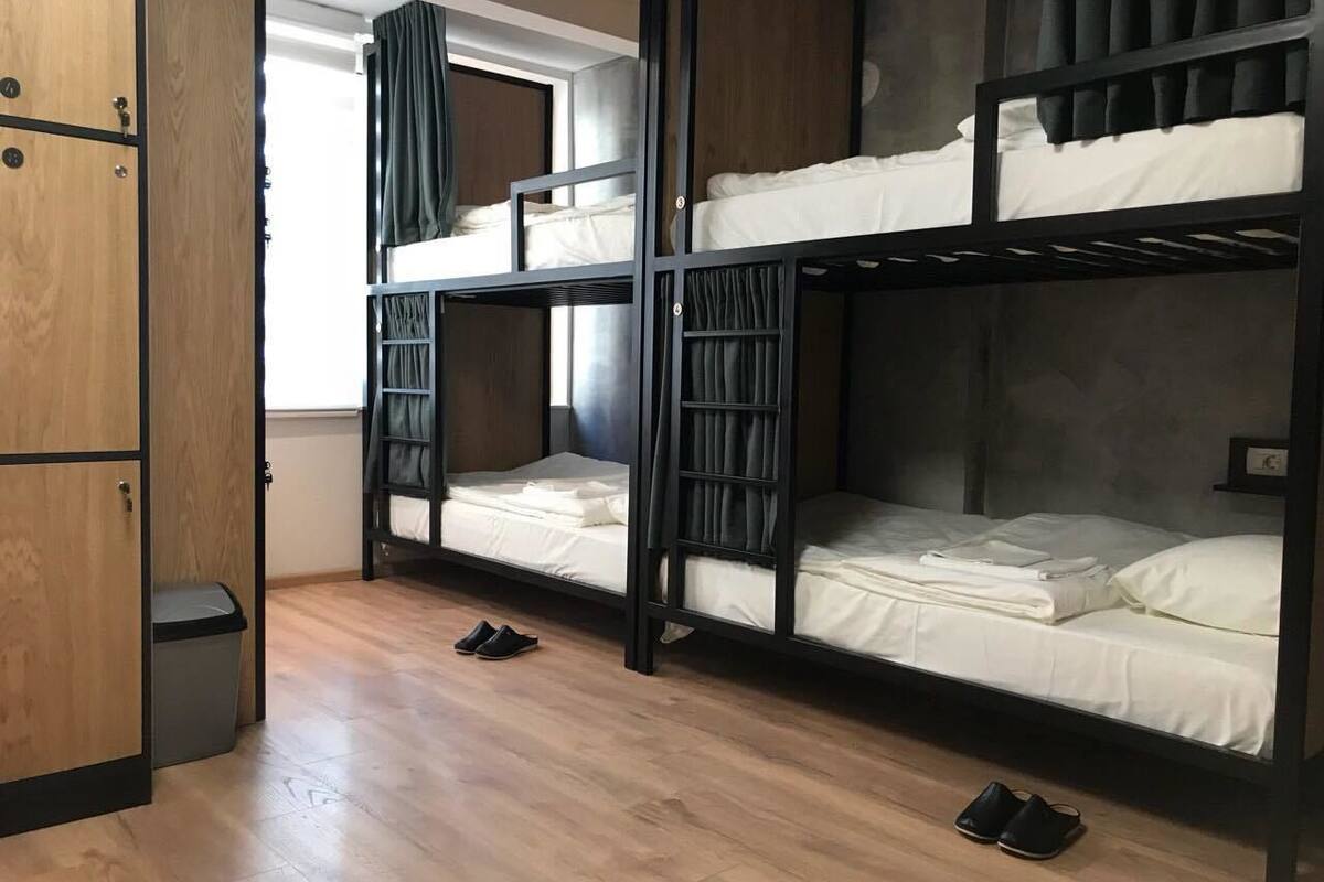 Un dormitorio con literas, un armario de madera, un cesto de basura y una ventana con cortinas.