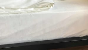A neatly made bed with white linens and a single pillow, a wall socket, and a power outlet on the wall. - Hostel Boulevard Prishtina (Pristina)
