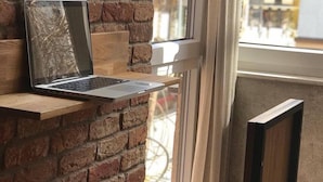 A laptop on a wooden shelf against a brick wall, a chair, and a view of the street through a window with curtains. - Hostel Boulevard Prishtina (Pristina)