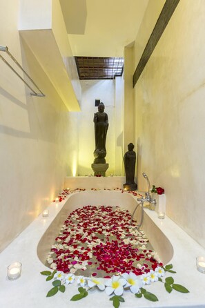 A bathtub filled with rose petals and candles, with a statue in the background.