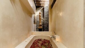 A narrow, stone-walled bathroom with a bathtub filled with rose petals and candles. - 2 Bedroom Villa in Seminyak Bali with private pool and enclosed Living Room. (Seminyak)