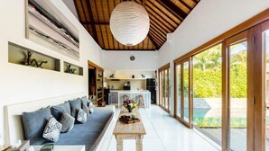 A modern interior with a sofa, a dining table, and a kitchen in the background. - 2 Bedroom Villa in Seminyak Bali with private pool and enclosed Living Room. (Seminyak)