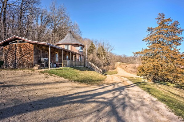 A rustic cabin with a wrap-around porch, a chimney, and a dirt path leading to it.