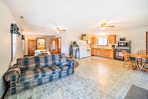 A living room with a blue plaid sofa, a dining area with a wooden table and chairs, and a kitchen with wooden cabinets and appliances.