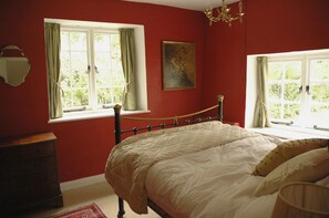 A bedroom with two windows, a bed, a dresser, and a chandelier. - 16th Century Thatched Cottage in an Acre of Mature Gardens (Bideford)