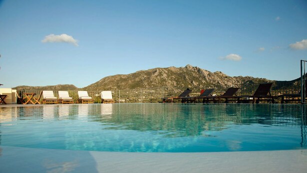 Una piscina con sillas de descanso y montañas al fondo.