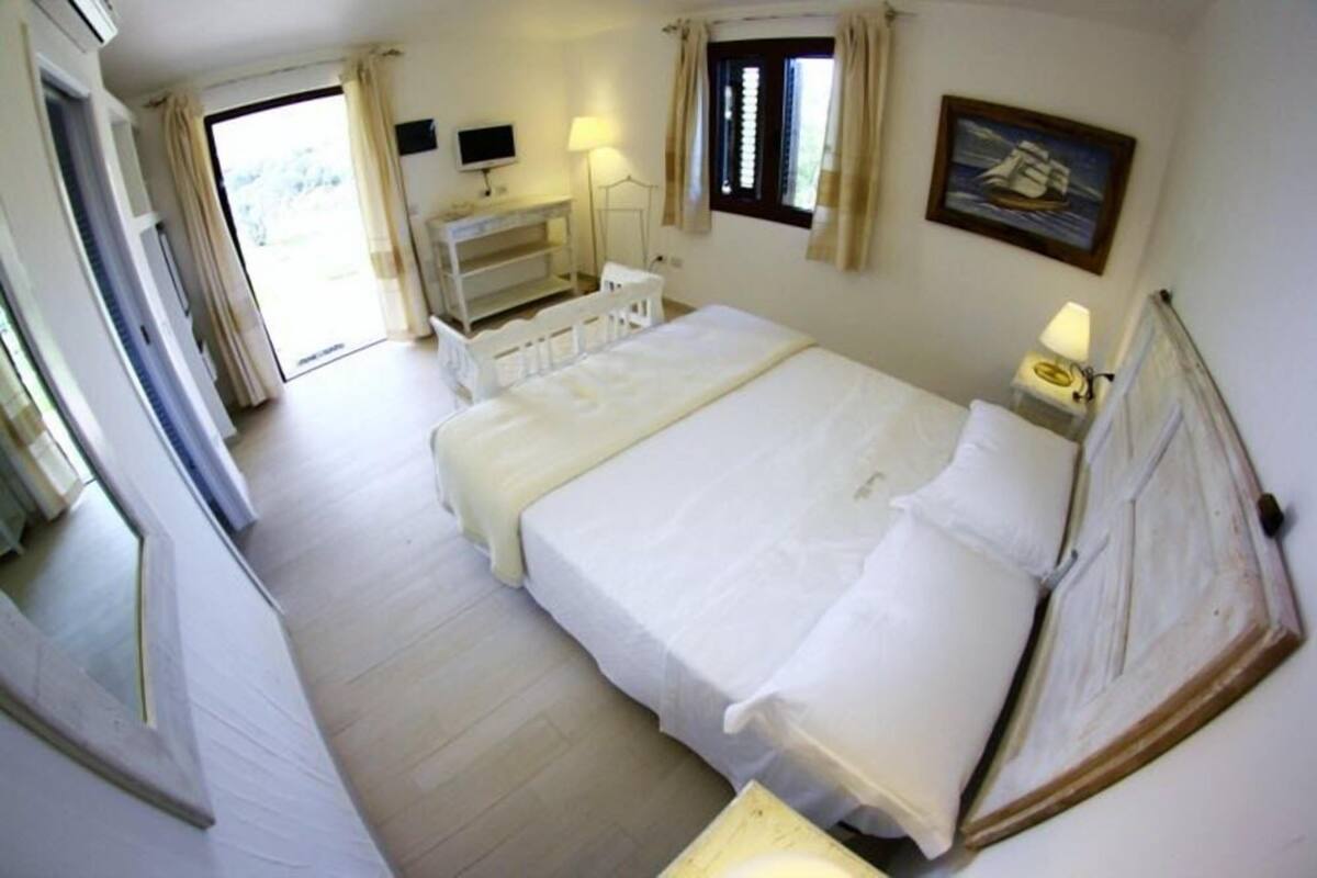A hotel room with a bed, bedside table, lamp, and a painting on the wall.