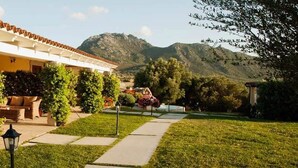 Un hotel con un patio cubierto, un jardín con un sendero y montañas al fondo.