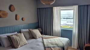 Un dormitorio con cama, almohadas, manta, una silla y ventana con cortinas.