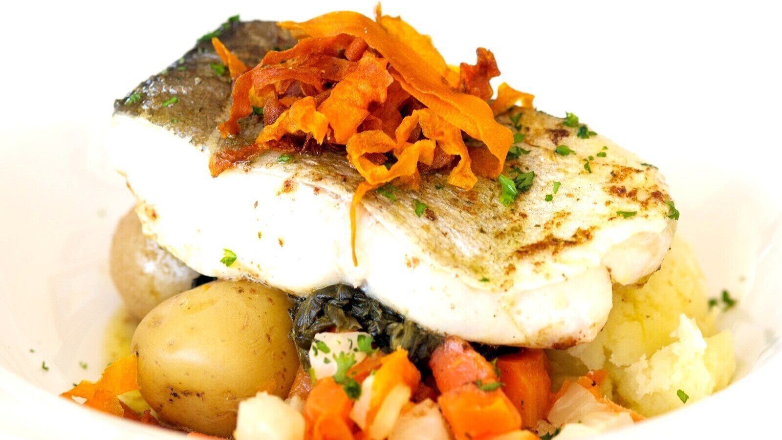 A dish with fish, potatoes, and carrots.