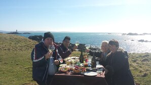 Un grupo de personas sentadas a una mesa con vista al mar y un faro al fondo.