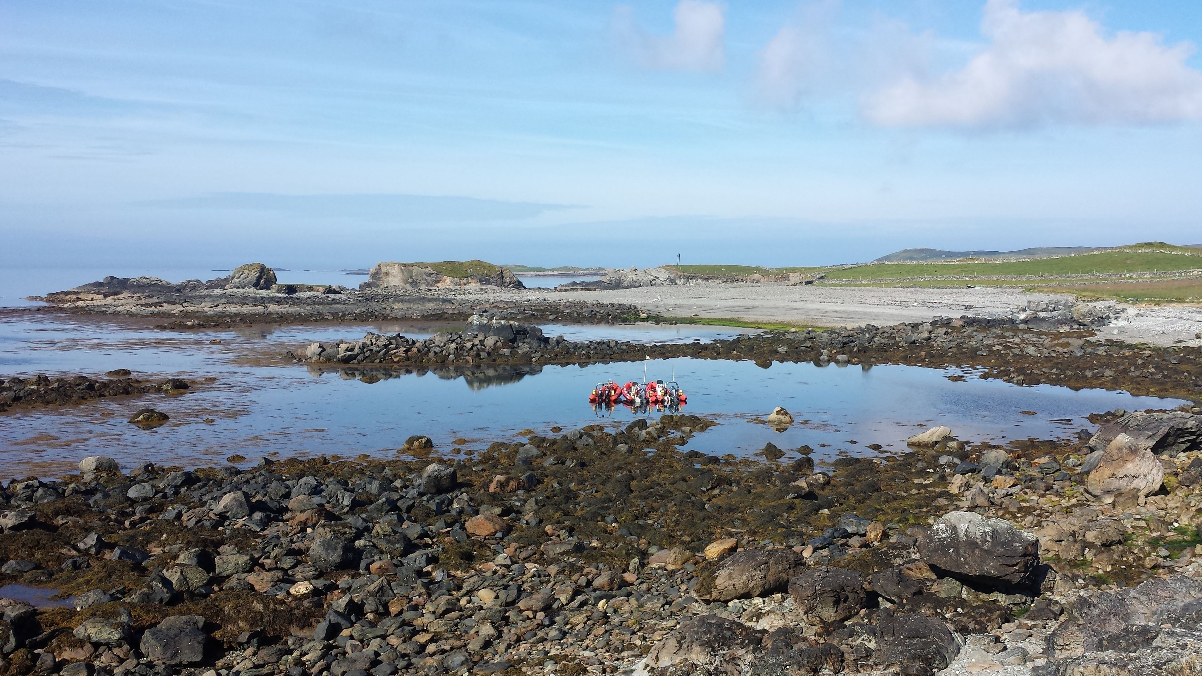 A rocky shoreline with a group of people in red uniforms gathered near a body of water.