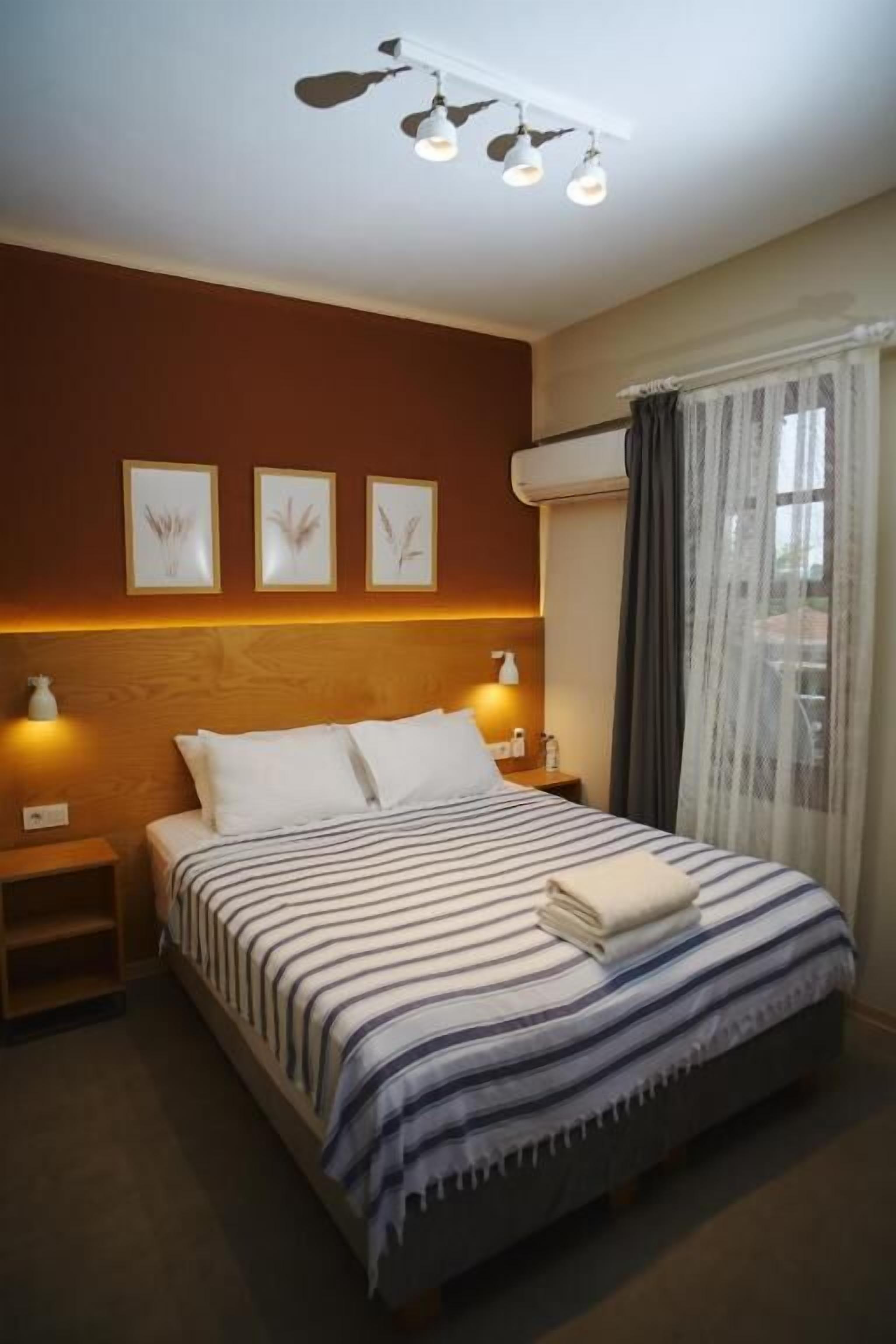 Una habitación de hotel con cama, lámparas de noche, mesita y cuadros en la pared.