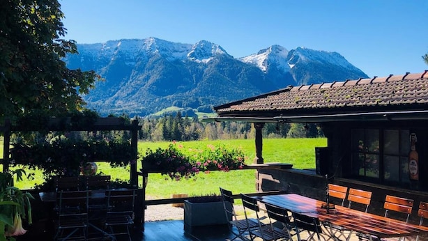 Una terraza de madera con mobiliario exterior, un pérgola con plantas trepadoras y vistas a la montaña.