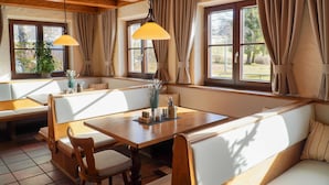 Un comedor acogedor con muebles de madera, ventanas amplias con cortinas y lámparas colgantes.