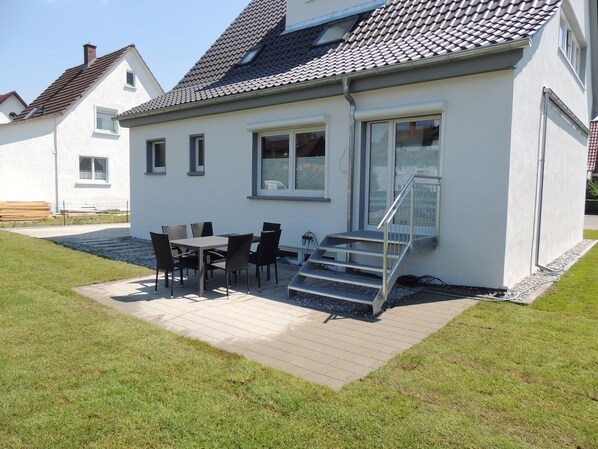 Une maison moderne dotée d’un patio, d’une table à manger avec des chaises et d’un escalier menant à l’entrée.