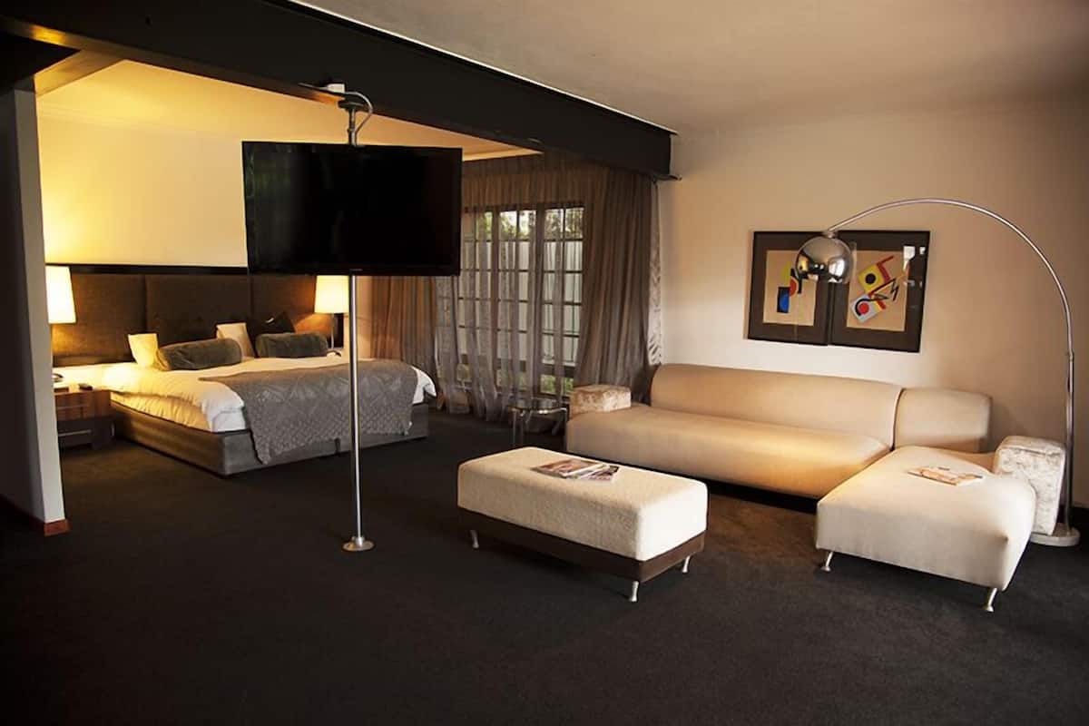 A hotel room with a bed, a sofa, a TV, and artwork on the wall.