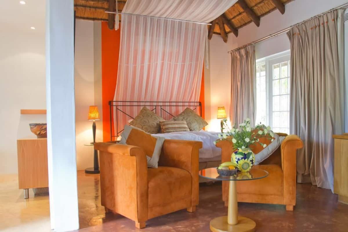 A bedroom with a bed, two chairs, a table, and a vase of flowers.