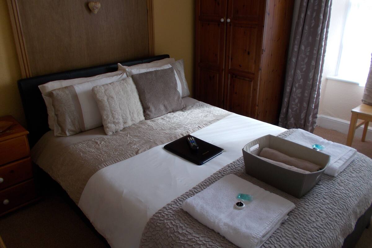 A neatly made bed with a remote control, a tray with toiletries, and a wooden wardrobe in a hotel room.