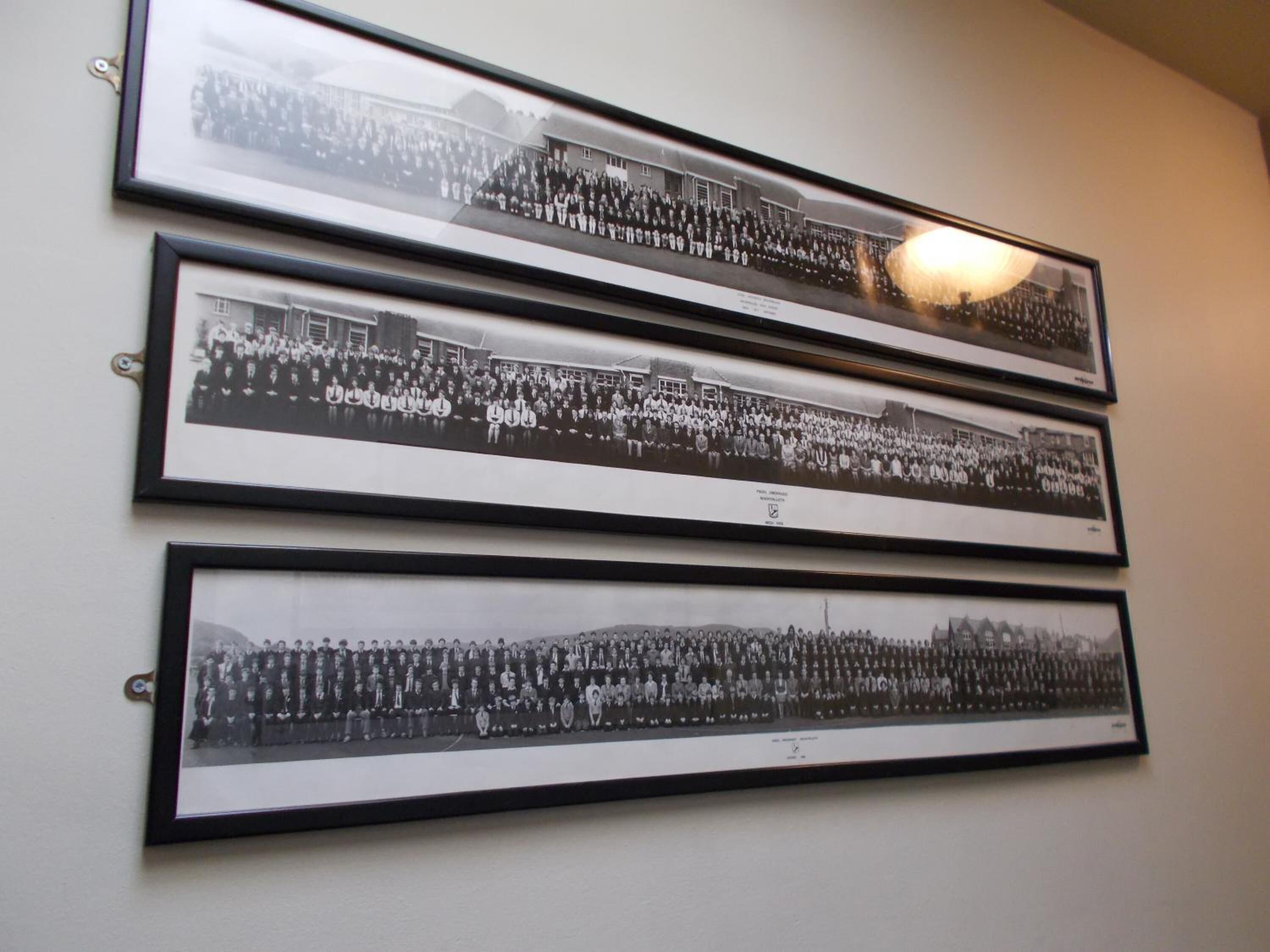 Three black and white framed photographs of groups of people, likely from a school or similar institution, displayed on a wall.