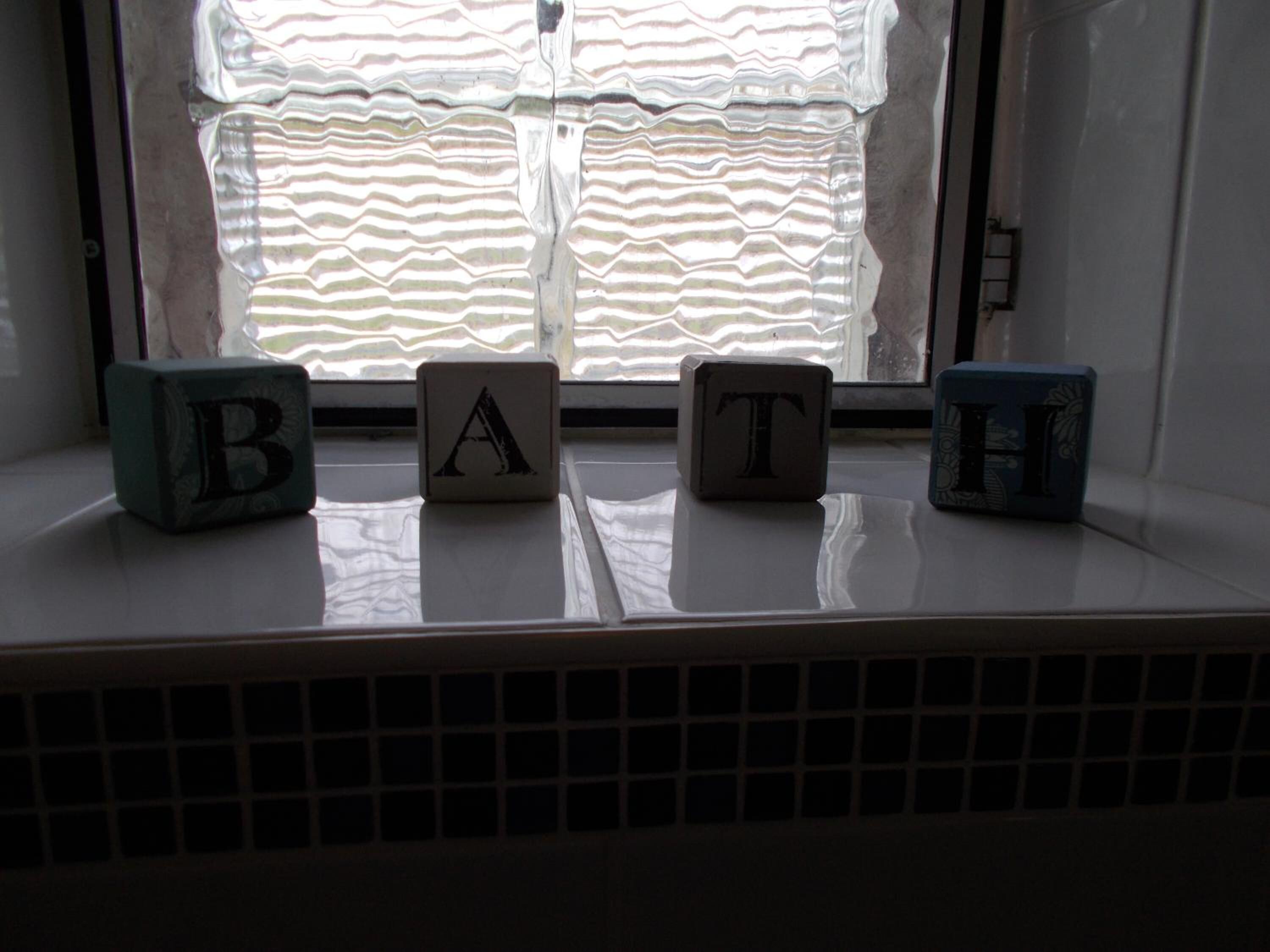 Quatre blocs de construction portant les lettres B, A, T, H, posés sur un rebord de fenêtre.