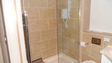 Un box de ducha con paredes de vidrio, un cabezal de ducha manual, un inodoro y un lavamanos.