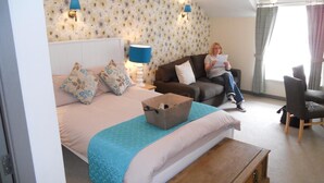 A hotel room with a bed, a wooden nightstand, a blue lamp, a sofa, and a chair. - The White Lion Hotel (Machynlleth)