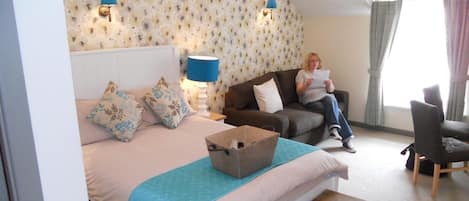 A hotel room with a bed, a wooden nightstand, a blue lamp, a sofa, and a chair.