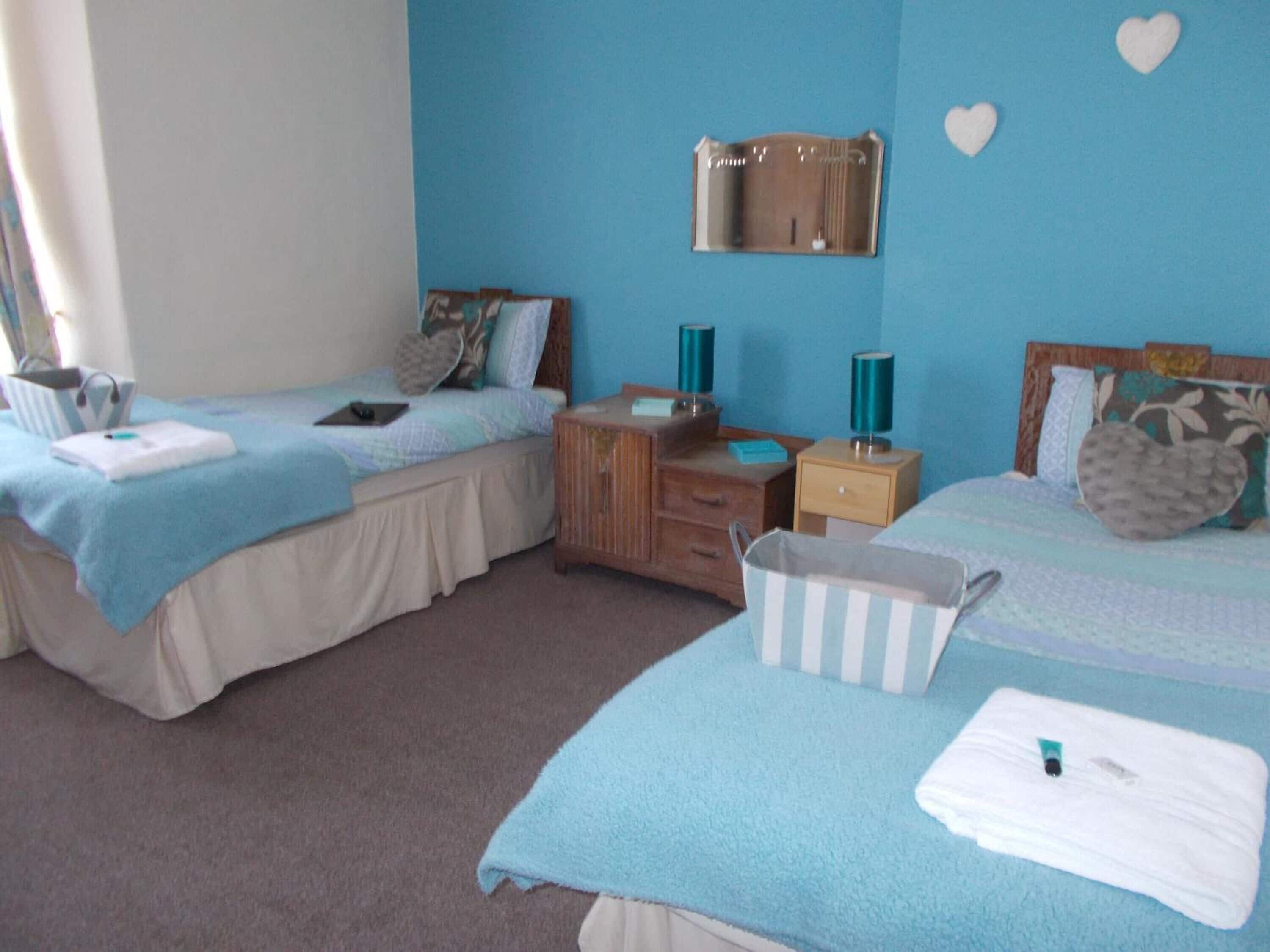 A bedroom with two beds, a wooden dresser, a nightstand, and a mirror.