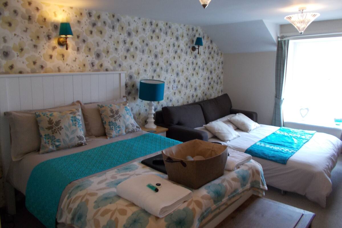 A hotel room with a bed, a sofa, a small table, and a window with curtains.