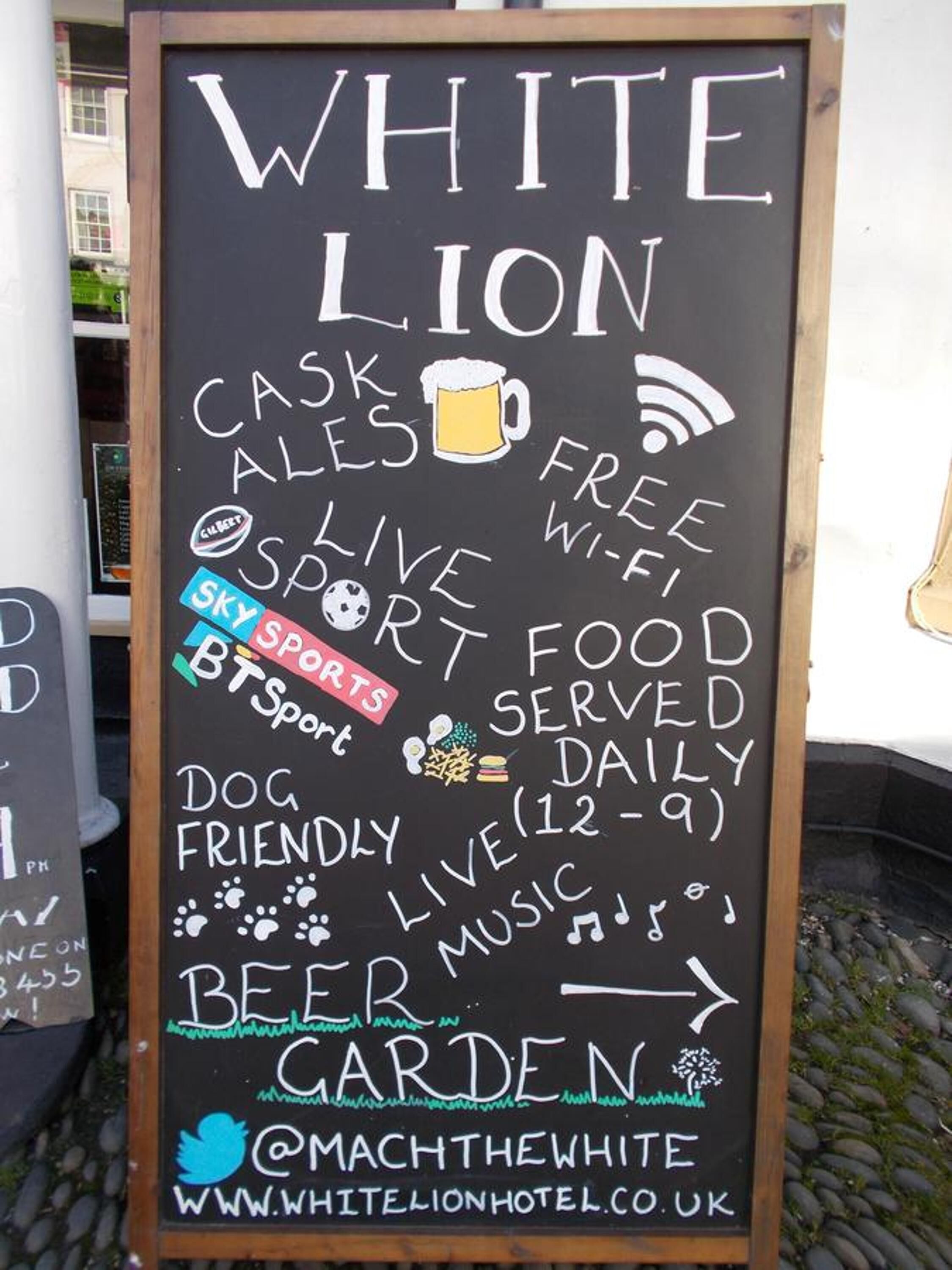 Een bord met krijt dat de faciliteiten van Hotel White Lion aankondigt, zoals biertjes van fust, gratis Wi-Fi, live sport, eten bij biertjes, honden toegestaan, live muziek en een tuin.