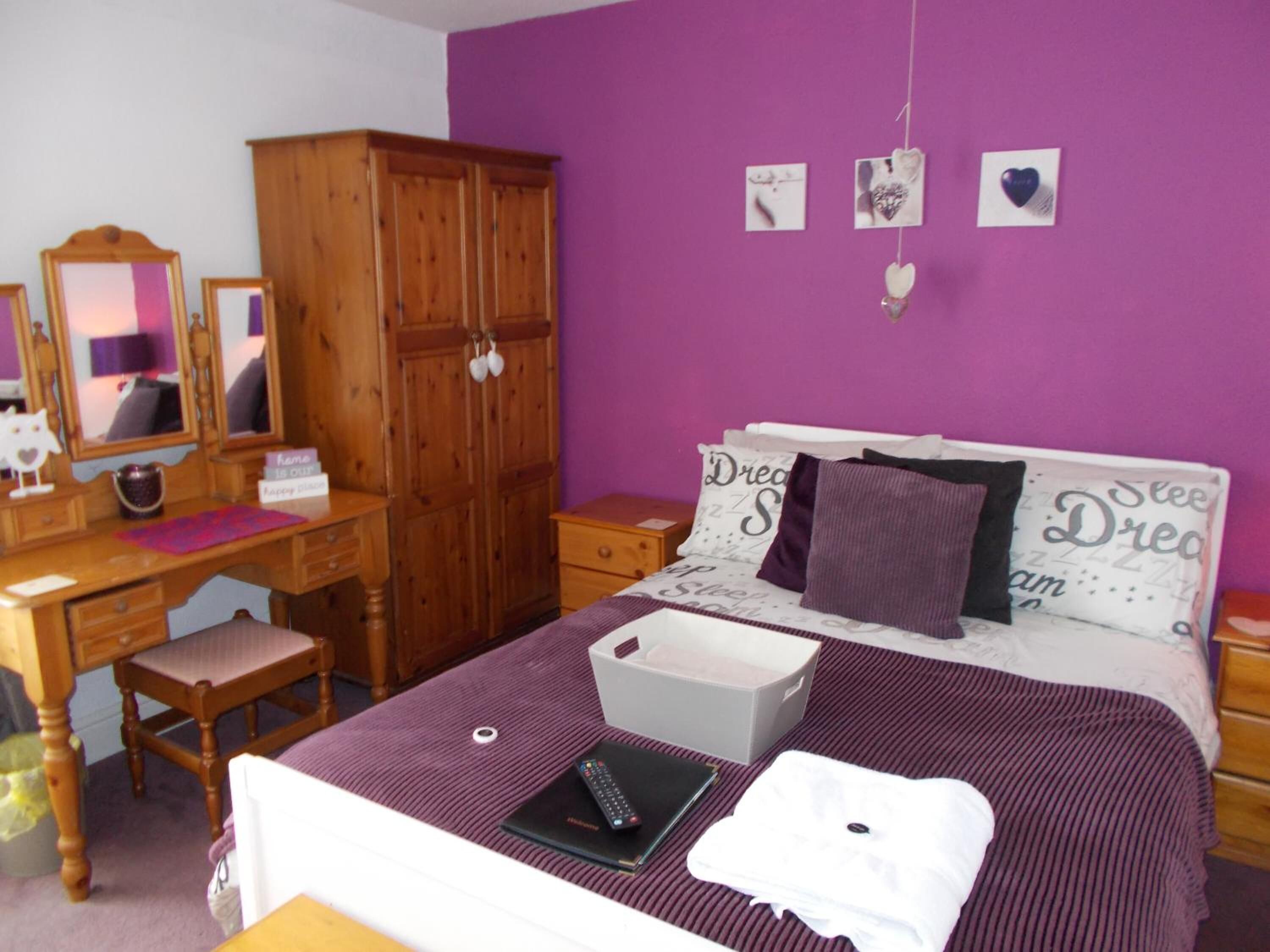 Un dormitorio con cama, armario de madera, escritorio con espejo y cómoda.