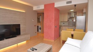 Een moderne woonkamer met een flatscreen televisie, een bank, een salontafel en een eethoek met gele stoelen.