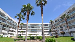 Een modern, meerhoog hotel met balkons, palmbomen en een verzorgd gazon.