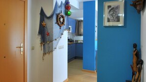 Um corredor com piso de madeira, parede azul decorativa, uma porta e uma área de cozinha ao fundo.