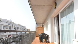 Uma varanda com mesa e cadeiras, uma porta de madeira e vista para edifícios ao fundo.