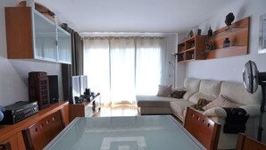 Uma sala de estar com uma mesa de jantar de vidro, um sofá, uma televisão e uma estante de livros.