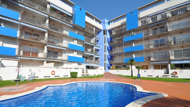 Um hotel moderno com piscina central, várias varandas e céu claro.