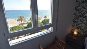 Ein Zimmer mit Blick auf einen Strand, ein Sessel und ein Nachttisch mit Lampe.