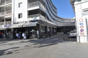 A modern building with a curved facade, a ground-level retail space with clothing items on display, and a car parked in front.