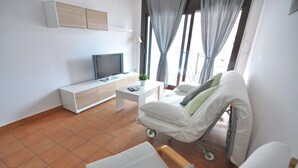 Een moderne hotelkamer met een bed, een televisie, een klein wit tafeltje en een raam met gordijnen.