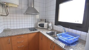 Een keuken met witte betegelde muren, een roestvrijstalen spoelbak, een magnetron en een blauwe afwasschaal.
