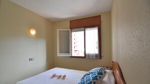 A small, single-bed room with a window, a wall-mounted light, and a power outlet. - Vacation rental in Roses, Costa Brava: Cozy apartment 400 meters from the beach, capacity for 4 people, with terrace and amenities. (Rosas / Roses)