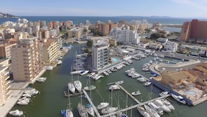 A marina with numerous boats docked, surrounded by multi-story buildings and a clear view of the sea.