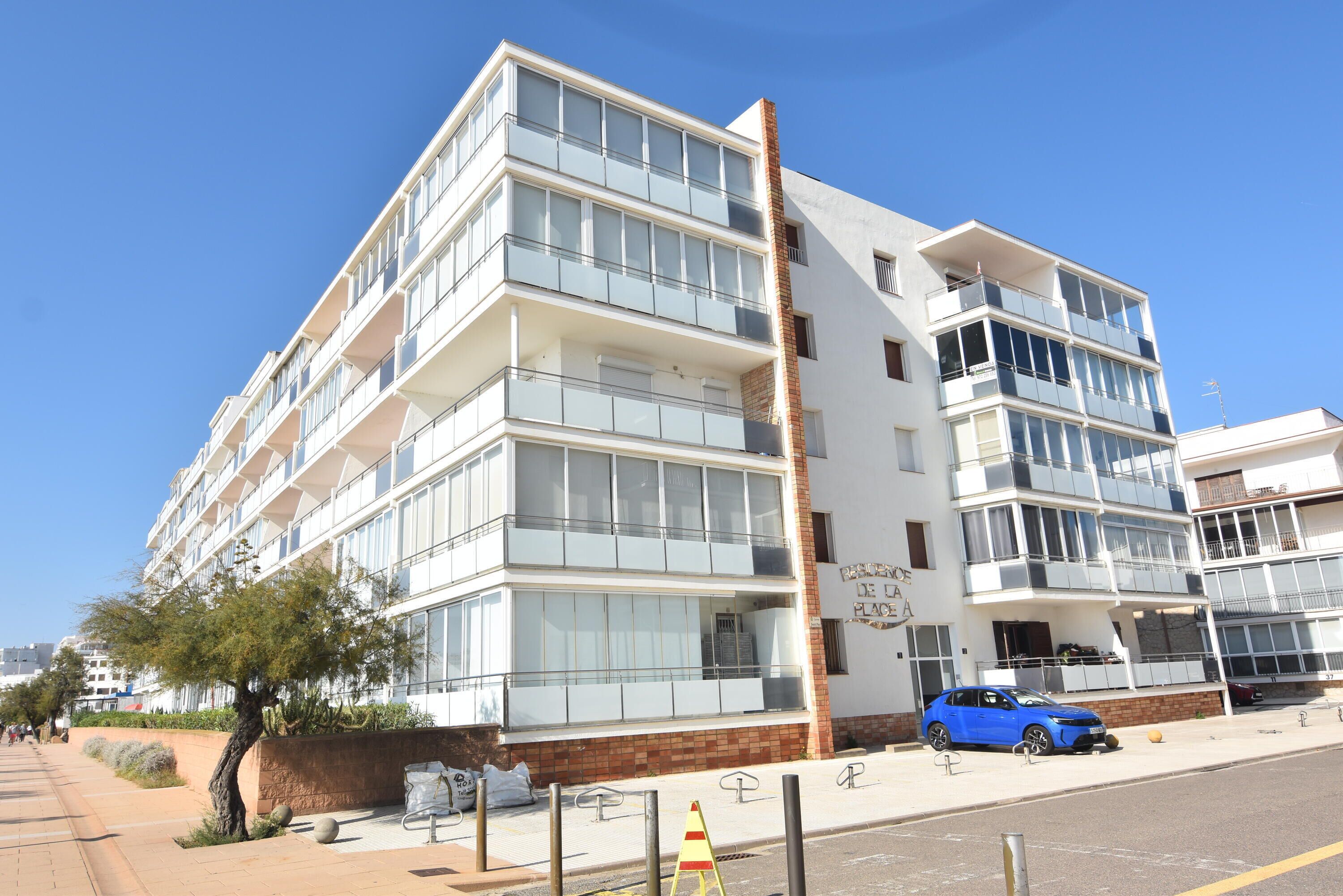 A multi-story hotel with balconies, a parking area, and a clear sky.