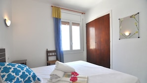 A neatly made bed with a blue and white pillow, a folded towel, and a book with pink flowers. - Charming apartment for rent in Roses, Costa Brava! Ideal for 5 people, just 10 meters from the beach. Book now! (Rosas / Roses)