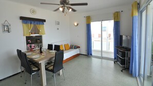 A modern room with a dining table, chairs, a sofa, a ceiling fan, and a sliding glass door with curtains. - Charming apartment for rent in Roses, Costa Brava! Ideal for 5 people, just 10 meters from the beach. Book now! (Rosas / Roses)