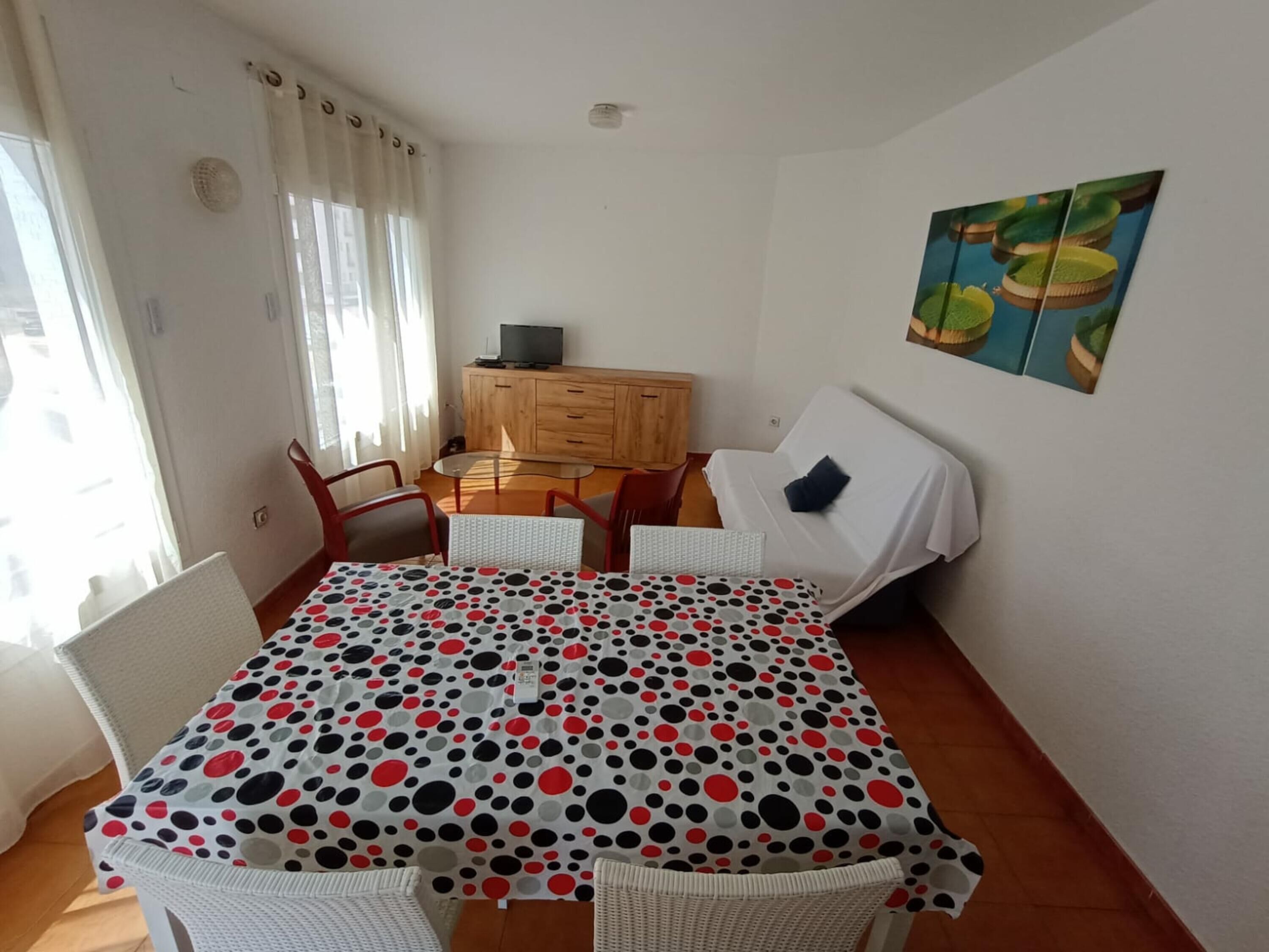 Una habitación con una mesa de comedor cubierta por un mantel a lunares, un sofá, un mueble de madera y un cuadro en la pared.