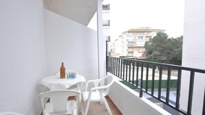 A balcony with a small table and chairs, a bottle, and a view of buildings and greenery. - Enjoy your Vacation in this Cozy Apartment in Roses, Costa Brava! Just a few steps from the beach and with all the amenities you need. (Rosas / Roses)